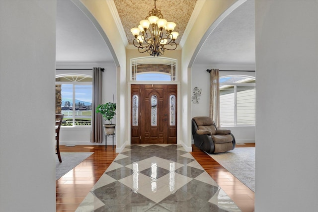 foyer with ornamental molding, a healthy amount of sunlight, a notable chandelier, and arched walkways