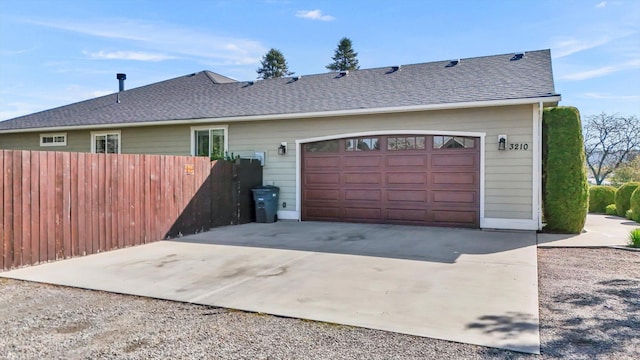 exterior space with driveway, fence, roof with shingles, and a garage