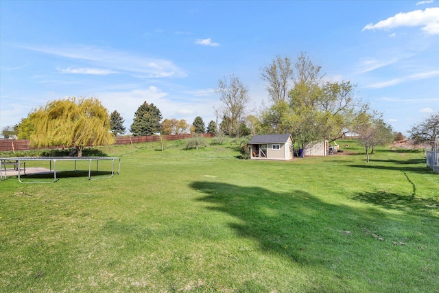view of yard featuring fence, an outbuilding, a shed, and a trampoline