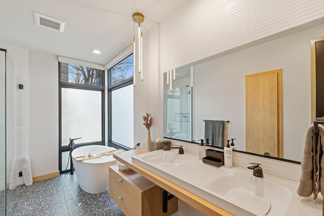 bathroom with a sink, double vanity, visible vents, baseboards, and a freestanding tub