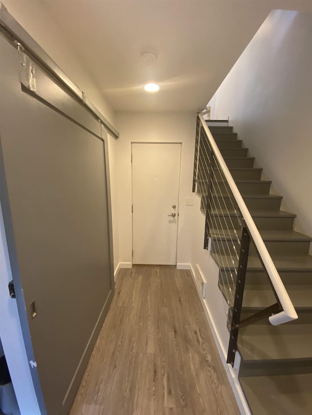 hallway featuring visible vents, a barn door, wood finished floors, baseboards, and stairs