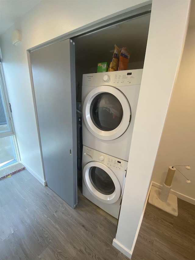 clothes washing area featuring baseboards, stacked washer / drying machine, wood finished floors, and laundry area