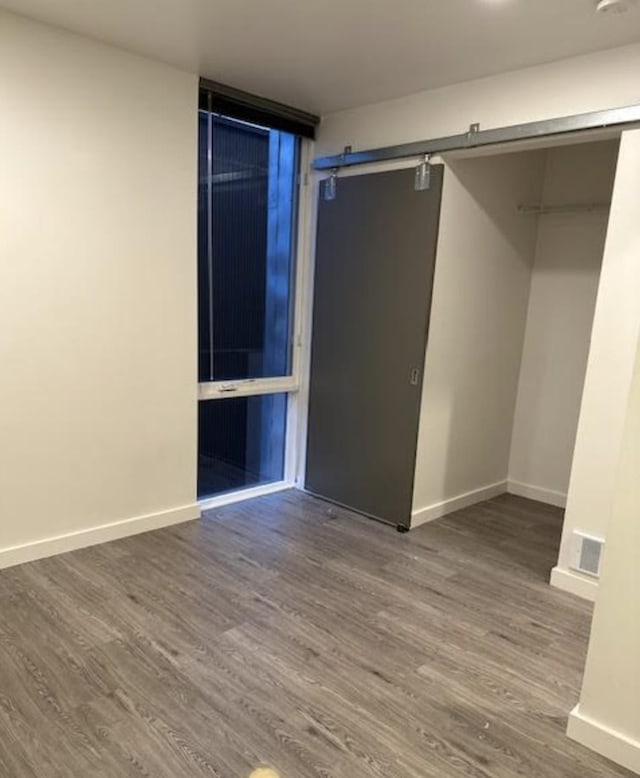 unfurnished bedroom with baseboards, a barn door, and wood finished floors