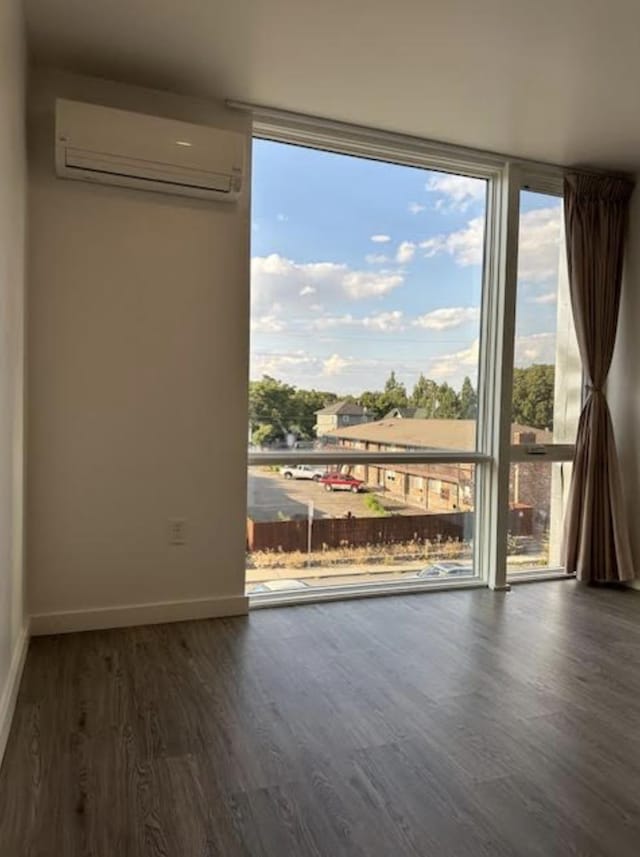 unfurnished room featuring an AC wall unit, wood finished floors, a healthy amount of sunlight, and expansive windows