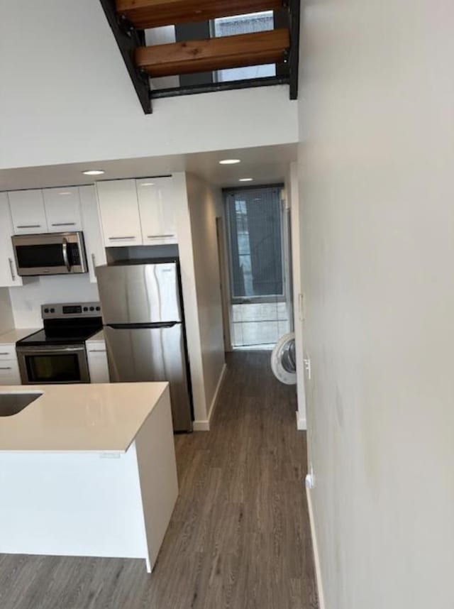 kitchen featuring a towering ceiling, baseboards, dark wood-style floors, white cabinetry, and stainless steel appliances