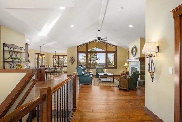living room featuring wood-type flooring, lofted ceiling, baseboards, a tile fireplace, and a ceiling fan