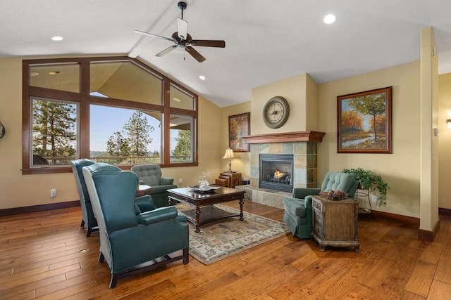 living room featuring baseboards, wood-type flooring, ceiling fan, and a tile fireplace