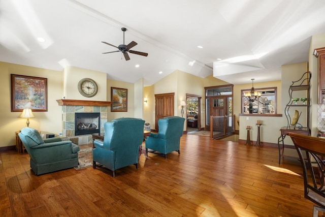 living area with a tiled fireplace, hardwood / wood-style flooring, baseboards, ceiling fan with notable chandelier, and lofted ceiling