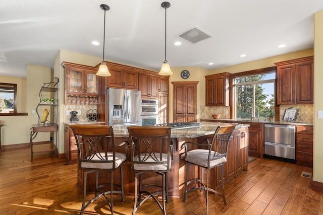 kitchen featuring decorative backsplash, a kitchen breakfast bar, appliances with stainless steel finishes, a center island, and light stone countertops