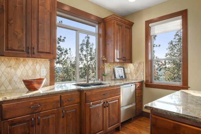 kitchen featuring stainless steel dishwasher, light stone counters, a sink, and light wood-style flooring