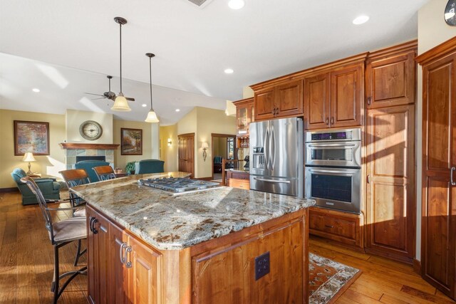 kitchen with light stone countertops, appliances with stainless steel finishes, a fireplace, a ceiling fan, and a kitchen island