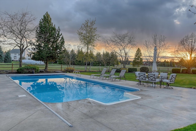 pool at dusk with a patio, a lawn, fence, and a fenced in pool