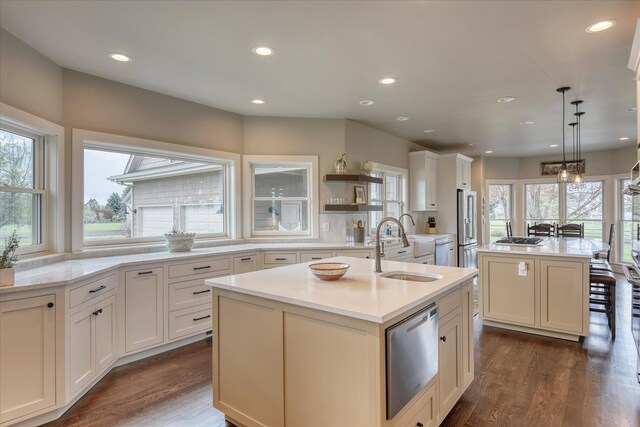 kitchen featuring a sink, light countertops, an island with sink, stainless steel appliances, and dark wood-style floors