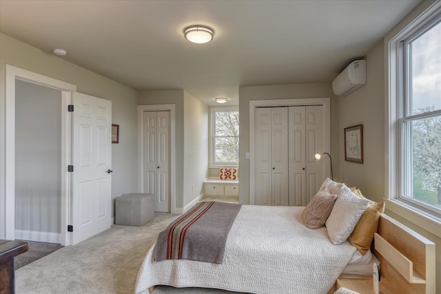 bedroom featuring multiple closets, baseboards, a wall unit AC, and carpet flooring