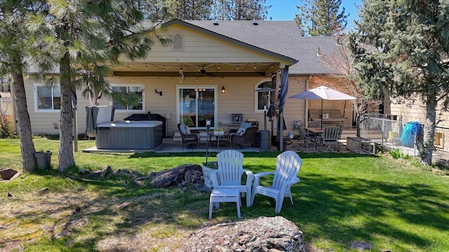 back of house with a hot tub, a patio, a ceiling fan, and a lawn
