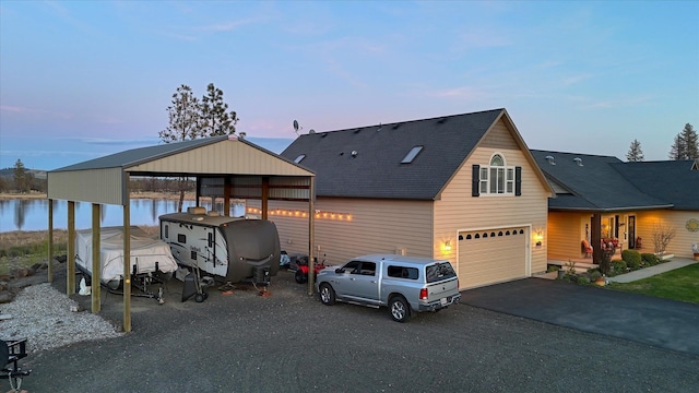 view of front of property with a shingled roof, a garage, a water view, a carport, and driveway
