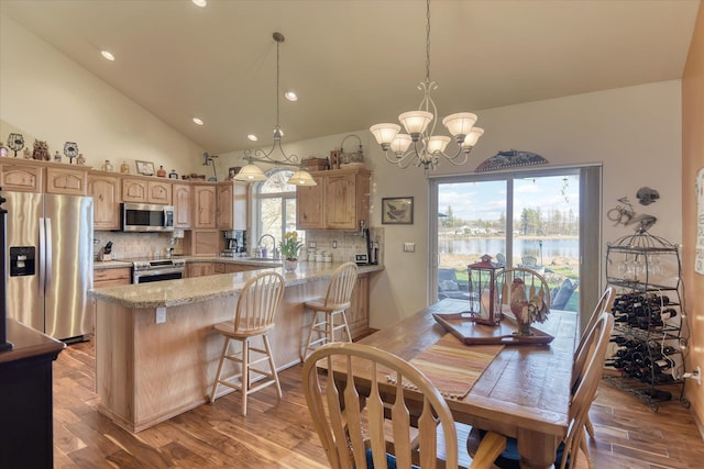 dining room with wood finished floors, high vaulted ceiling, an inviting chandelier, a water view, and recessed lighting