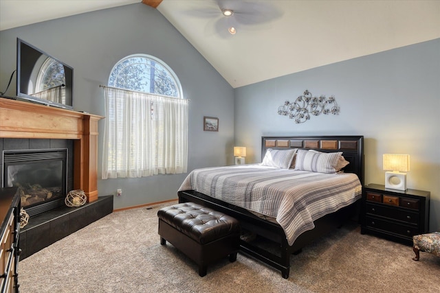 carpeted bedroom featuring a tiled fireplace, a ceiling fan, and high vaulted ceiling