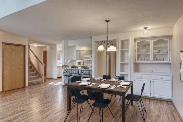 dining room featuring a textured ceiling, light wood finished floors, a chandelier, and stairway
