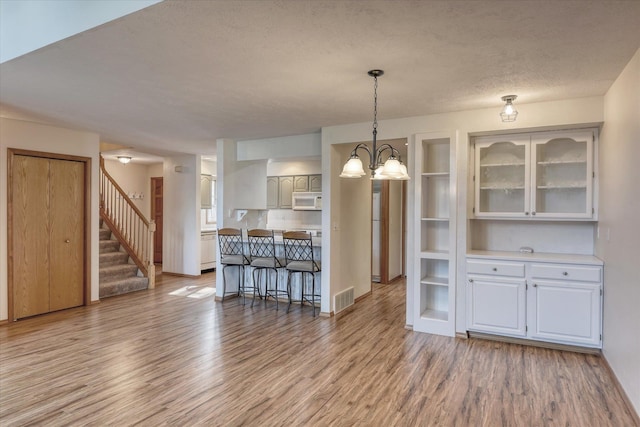 kitchen with glass insert cabinets, visible vents, white cabinets, white microwave, and light wood-style floors