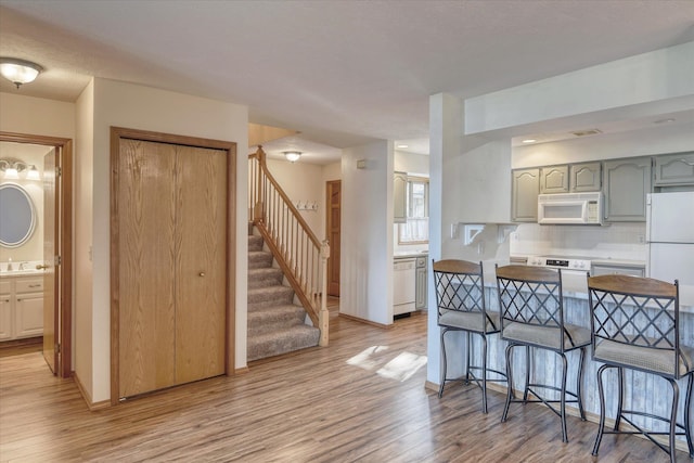kitchen featuring white appliances, backsplash, a breakfast bar, and light wood-style flooring