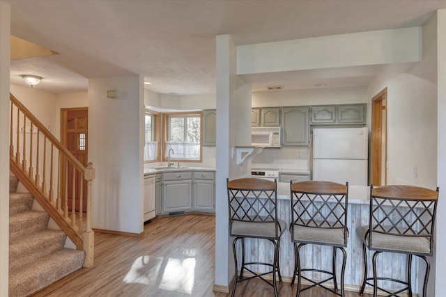 kitchen with light wood-style floors, a sink, gray cabinetry, and white appliances