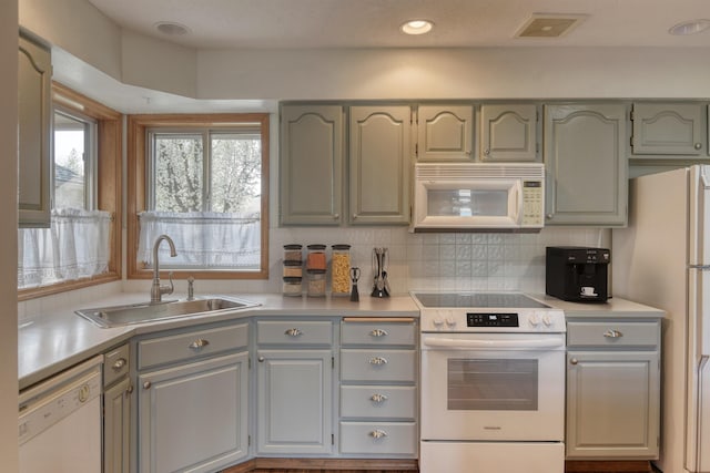 kitchen with gray cabinetry, a sink, visible vents, and white appliances