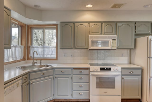 kitchen with decorative backsplash, white appliances, light countertops, a sink, and gray cabinetry