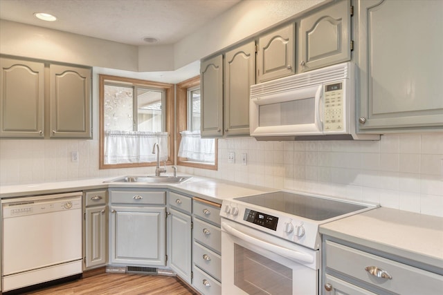 kitchen with a sink, white appliances, light countertops, tasteful backsplash, and gray cabinetry