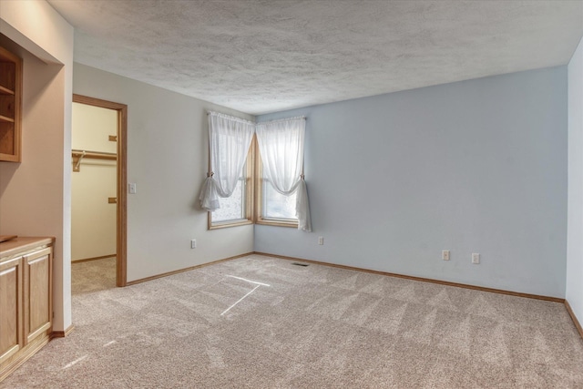 empty room featuring baseboards, light carpet, a textured ceiling, and visible vents