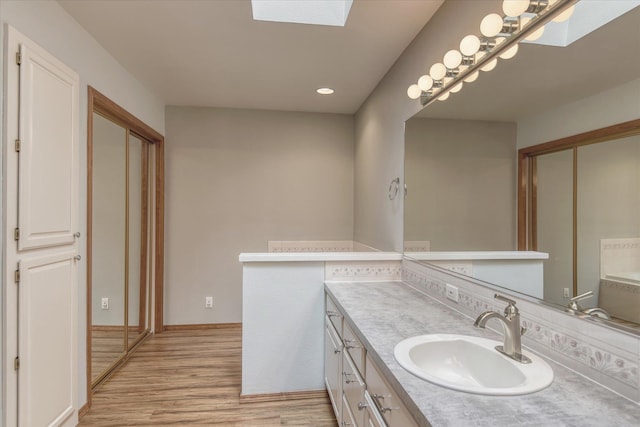 bathroom with a skylight, vanity, recessed lighting, and wood finished floors