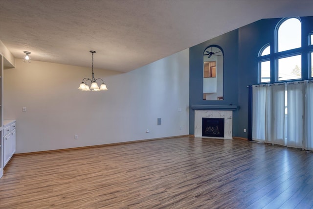 unfurnished living room featuring wood finished floors, a fireplace, baseboards, a textured ceiling, and a notable chandelier