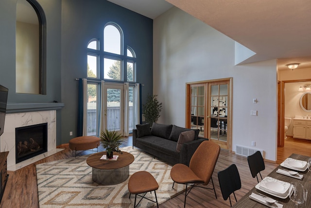 living room featuring visible vents, high vaulted ceiling, light wood-type flooring, a high end fireplace, and arched walkways