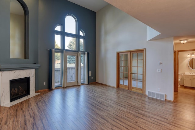 unfurnished living room featuring high vaulted ceiling, plenty of natural light, wood finished floors, and visible vents