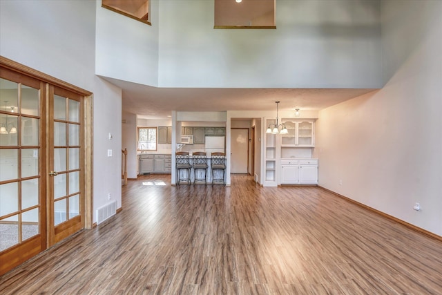 unfurnished living room featuring a high ceiling, visible vents, wood finished floors, and an inviting chandelier