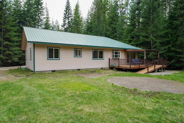 rear view of house with a lawn, a deck, a view of trees, and metal roof