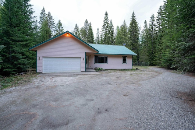 single story home featuring a view of trees, an attached garage, and metal roof