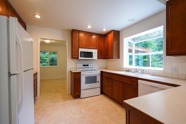 kitchen with brown cabinetry, a sink, light countertops, recessed lighting, and white appliances