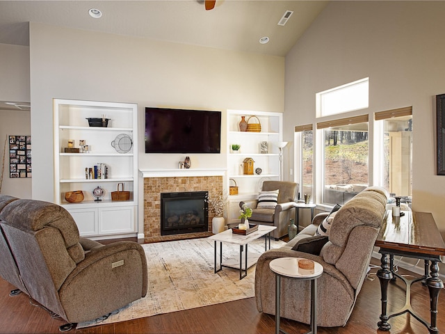 living room featuring dark wood-style flooring, a fireplace, built in shelves, and high vaulted ceiling