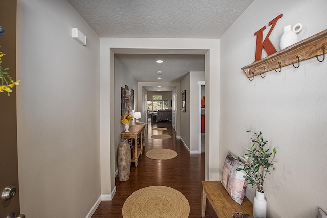 hallway featuring a textured ceiling, baseboards, and wood finished floors