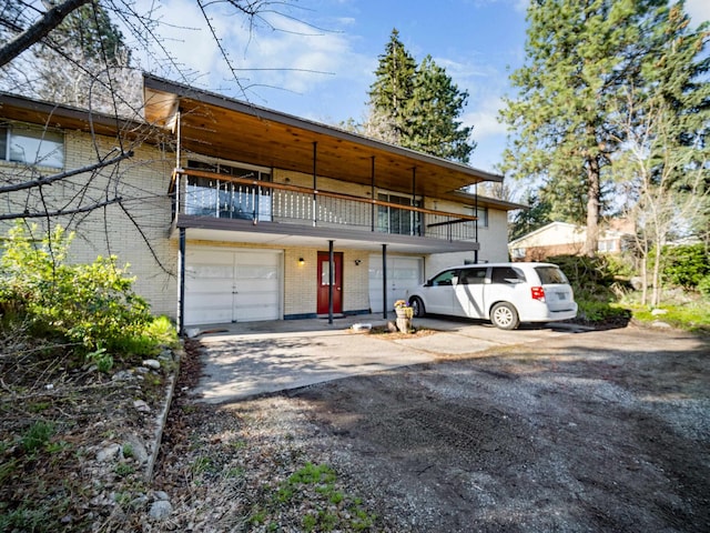 view of front of home featuring a garage, a balcony, driveway, and brick siding