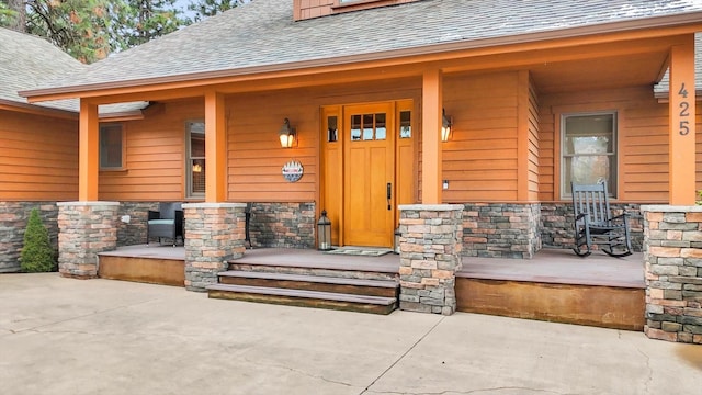 view of exterior entry featuring a shingled roof, covered porch, and stone siding