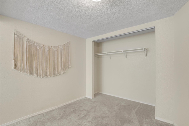 unfurnished bedroom with a closet, carpet flooring, a textured ceiling, and baseboards