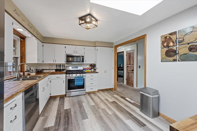 kitchen with a sink, stainless steel appliances, light wood finished floors, and white cabinetry
