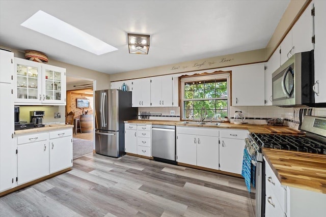 kitchen with tasteful backsplash, a sink, light wood-style flooring, appliances with stainless steel finishes, and a skylight