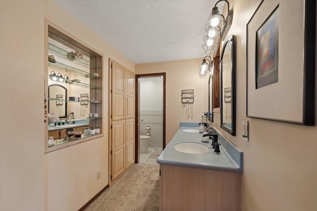 bathroom with a sink, a textured ceiling, toilet, and double vanity