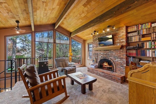 living area with ceiling fan, lofted ceiling with beams, a fireplace, carpet, and wooden ceiling