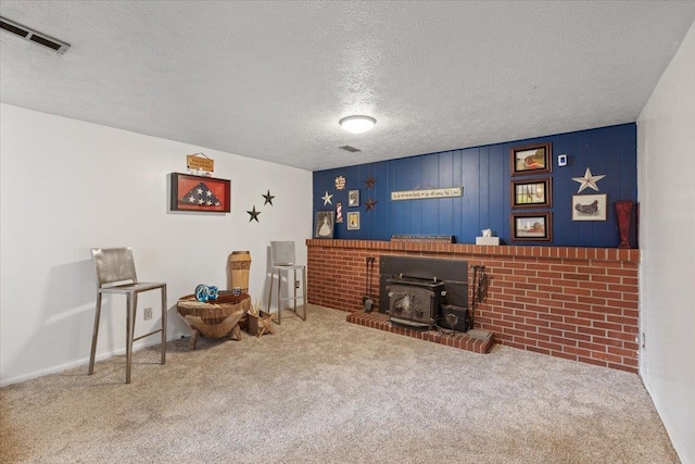 sitting room featuring carpet, a wood stove, a textured ceiling, and visible vents