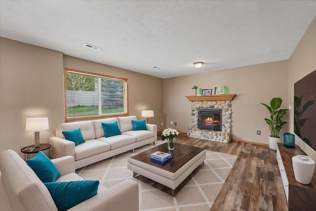 living area featuring visible vents, wood finished floors, baseboards, a stone fireplace, and a textured ceiling