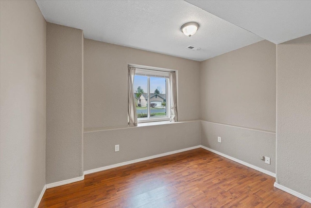 empty room with baseboards, a textured ceiling, wood finished floors, and visible vents